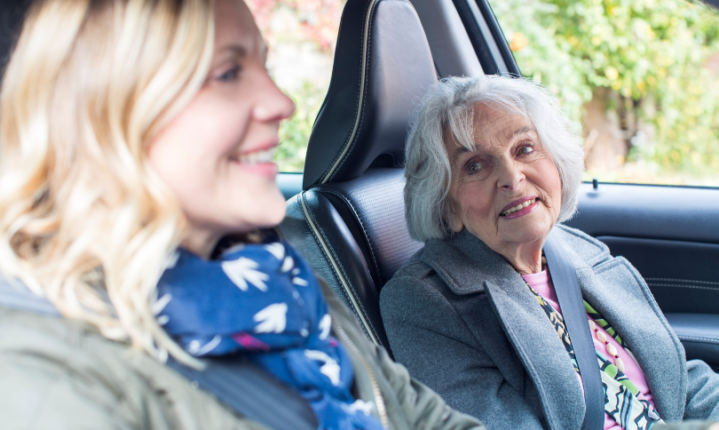 Female volunteer helping older woman into car